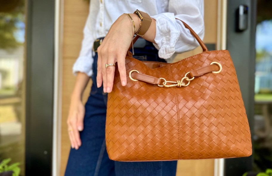 woman holding cognac satchel purse in front of house