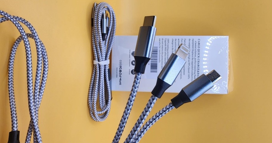 Three braided charging cables with USB-C, Lightning, and Micro-USB connectors are displayed on a yellow background. A packaged cable lies nearby.
