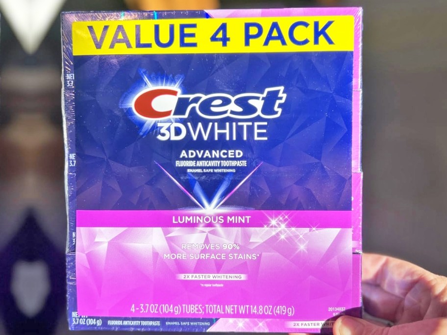 hand holding a 4-pack of Crest 3D White Advanced Toothpaste