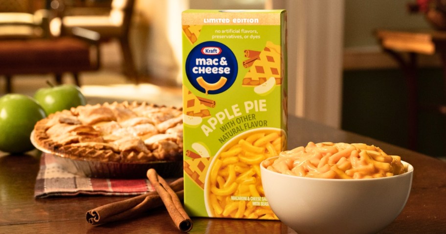 a box of Kraft Apple Pie Mac & Cheese next to a bowl of mac & cheese and an apple pie and apples on a table