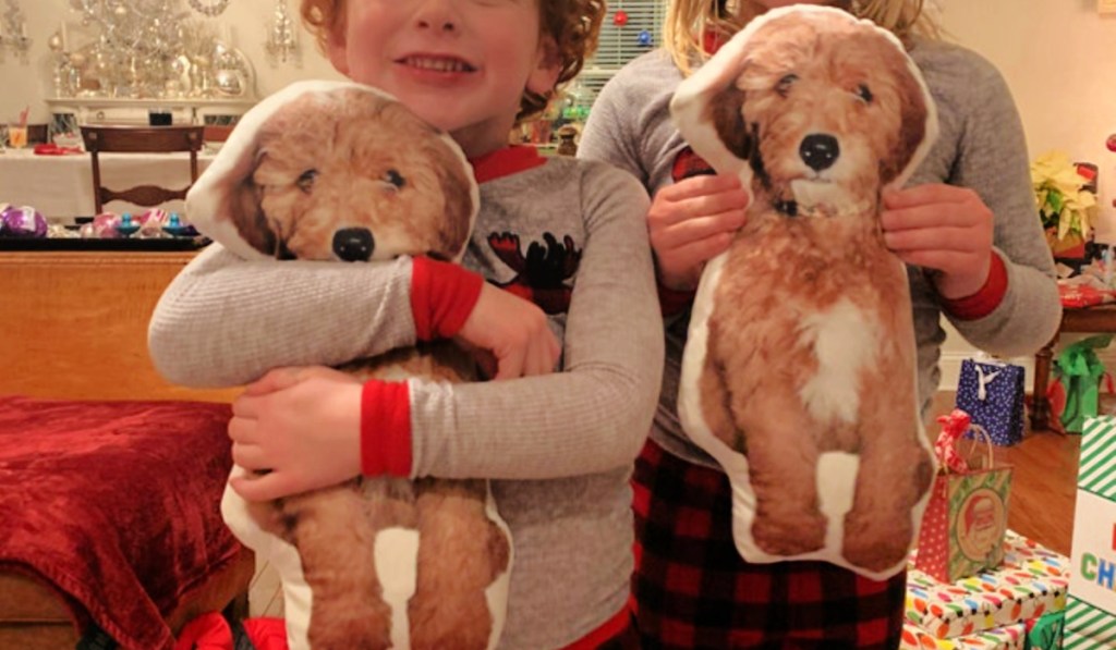 Two children holding 3-D pet pillows in front of Christmas tree