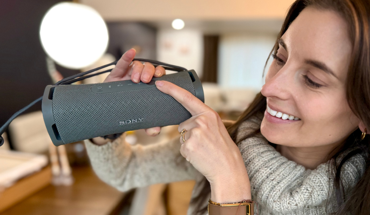 Woman holding gray Sony field speaker in hand and pushing button