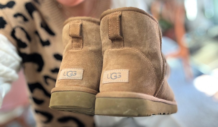 Woman holding brown UGG boots showing the back of the boot with the label