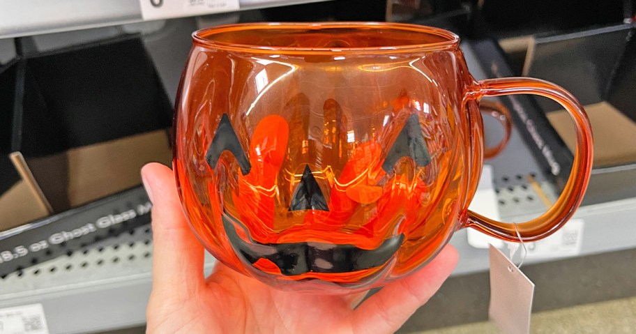 hand holding up an orange pumpkin shaped coffee mug