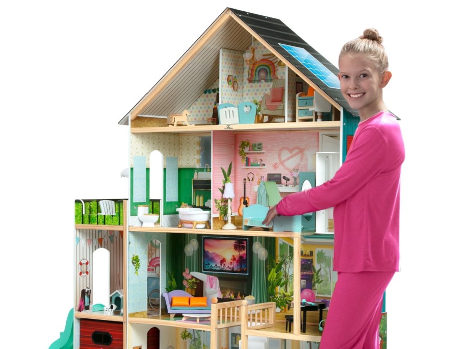 girl standing next to a large dollhouse