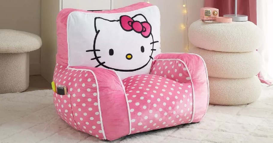 A plush pink armchair with white polka dots features a large Hello Kitty face on the backrest.
