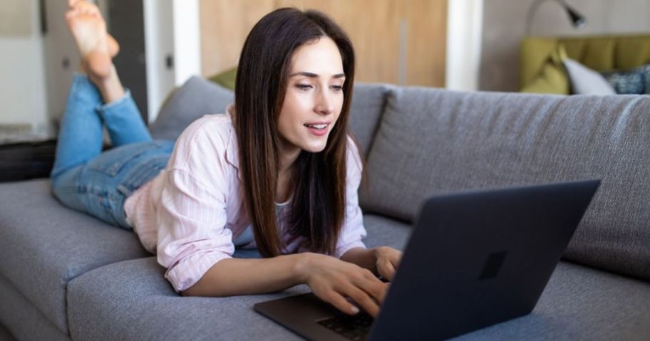 woman laying on couch and typing on laptop