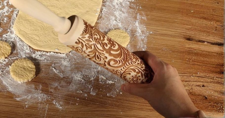 hand holding embossed rolling pin over dough