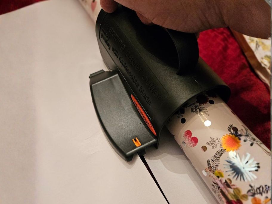 person using wrapping paper cutter to cute wrapping paper on table