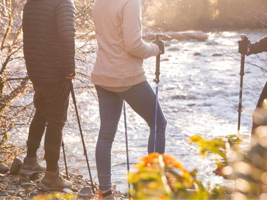 3 people near a stream with trekking poles