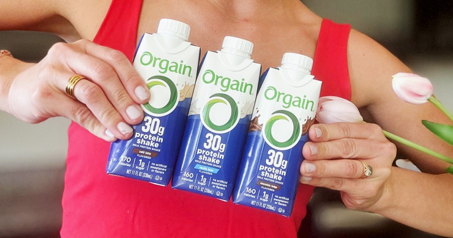 woman holding up 3 bottles of Orgain protein shakes