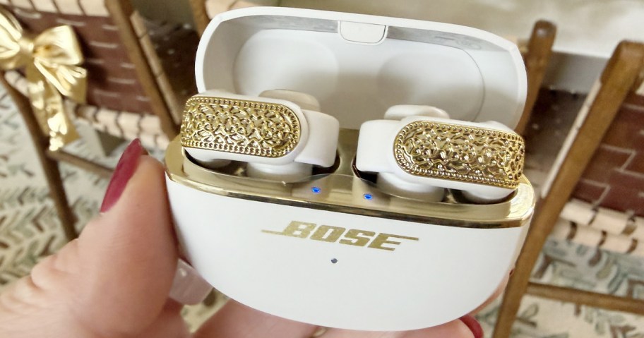 hand holding white and gold earbuds in case 