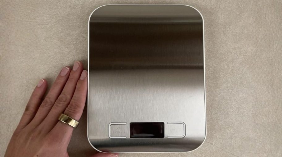 a womans hand next to a stainless steel digital food scale
