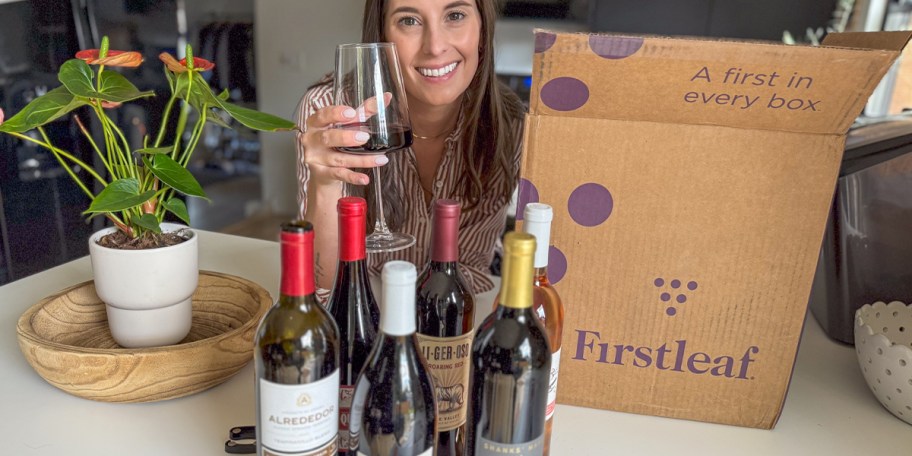 woman holding glass of wine with wine bottles on table