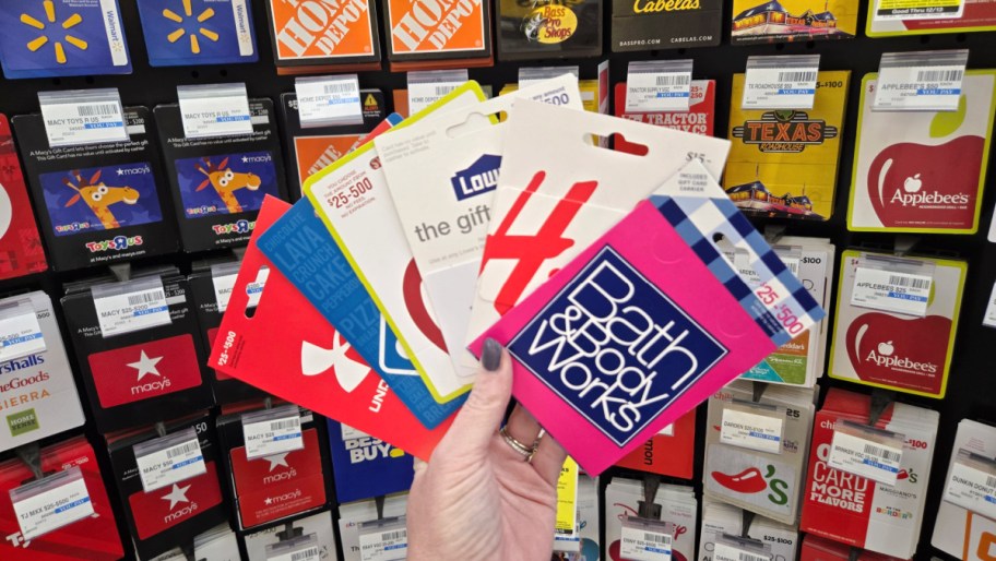 hand holding a fan of gift cards in front of a gift card display in a store