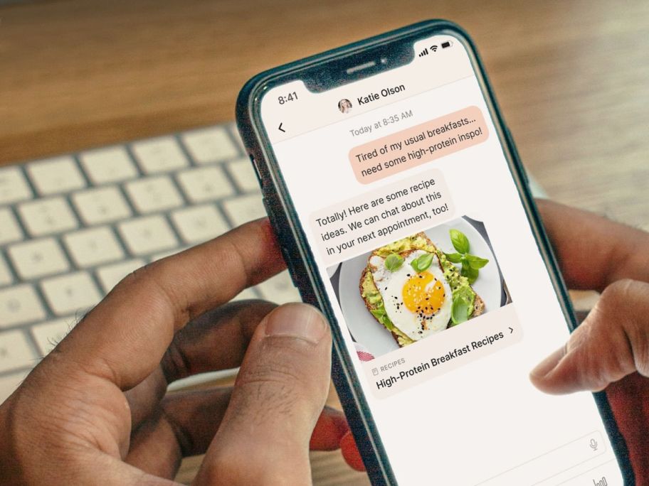 holding a phone showing a nutrition app in front of a keyboard