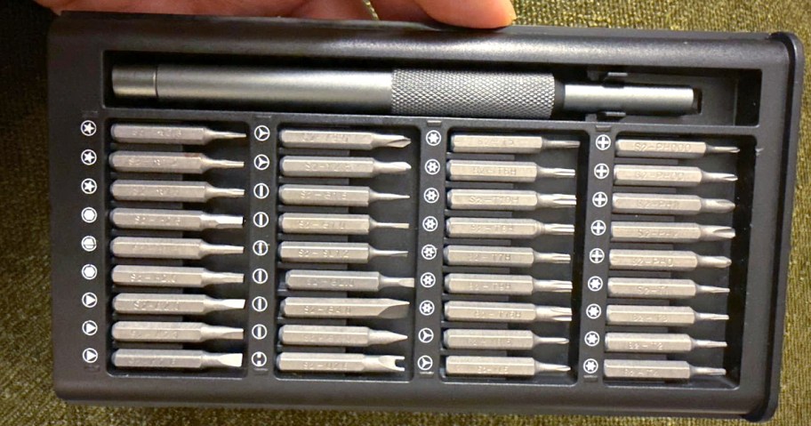 A black case containing a compact precision screwdriver kit. It includes a handle and various metal bits organized neatly in rows.