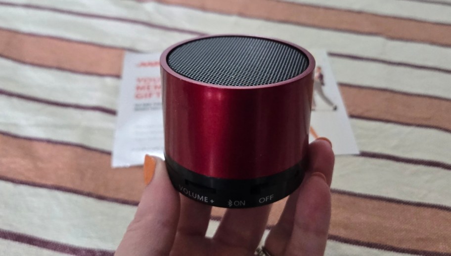 a womans hand holding a red bluetooth mini speaker