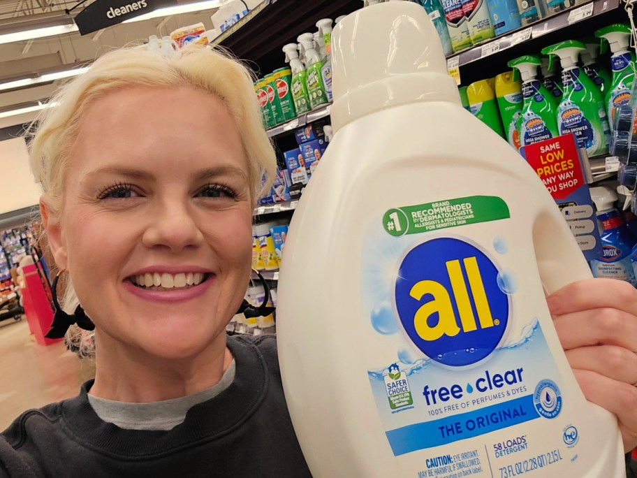 Woman holding up large bottle of all laundry detergent while standing in store aisle