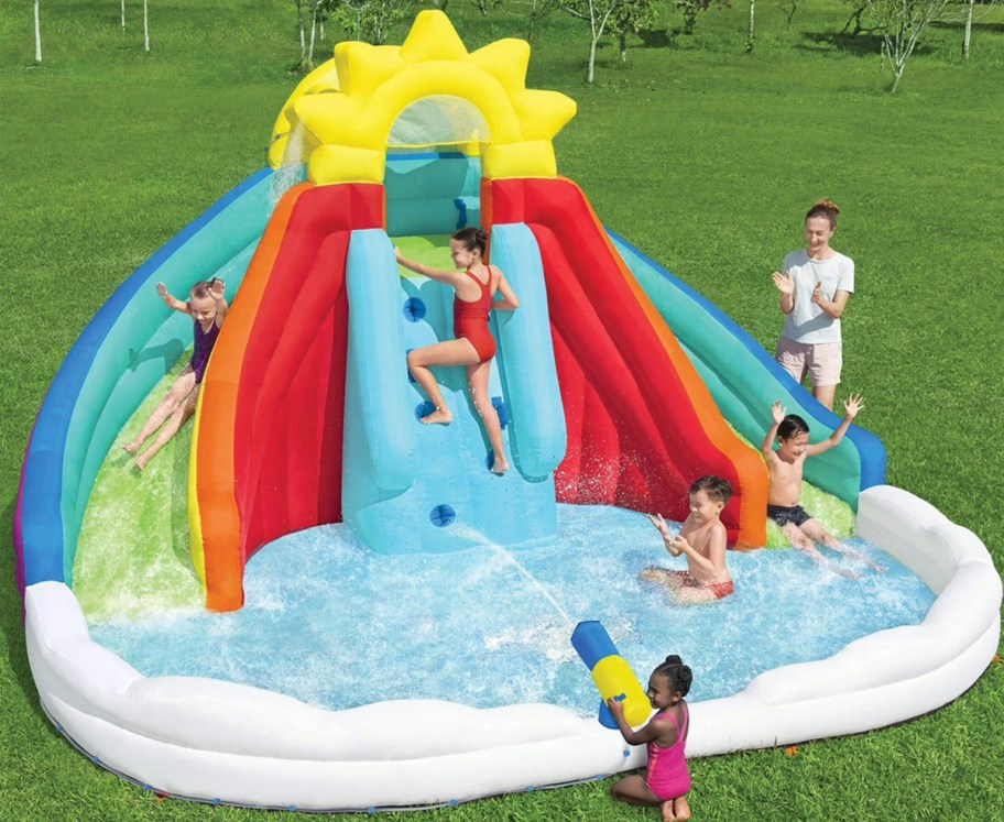 kids playing on a rainbow themed water slide in backyard