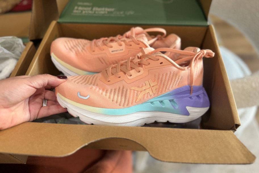 hand grabbing peach orange sneaker out of box