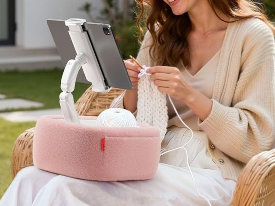 A woman crocheting with a fluffy tablet stand 