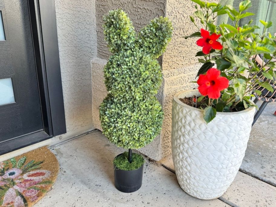 A large, green bunny topiary outside next to a potted plant