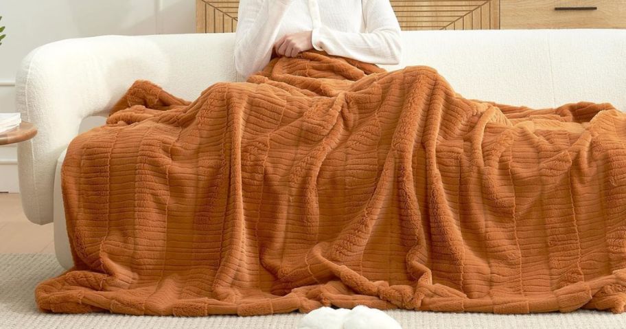 woman sitting on couch with orange blanket on her