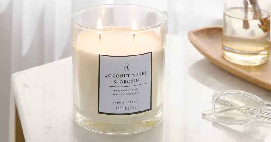 A lit "Coconut Water & Orchid" scented candle on a white countertop.