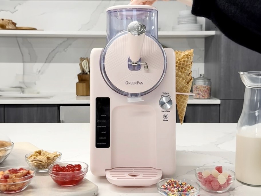 light pink ice cream maker on counter with bowls of toppings 