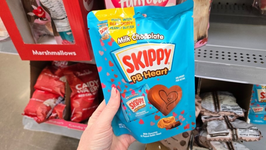 a womans hand holding a bag of skippy chocolate covered peanut butter hearts