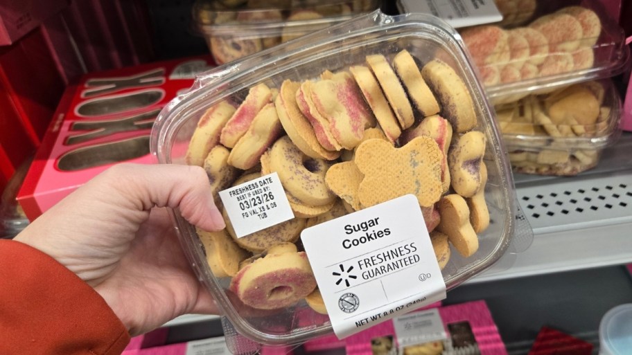 womans hand holding a container of valentines sugar cookies