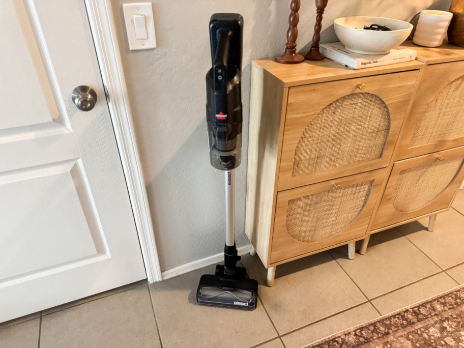 Cordless vacuum cleaner standing upright beside a light wood cabinet with four basket weave doors.