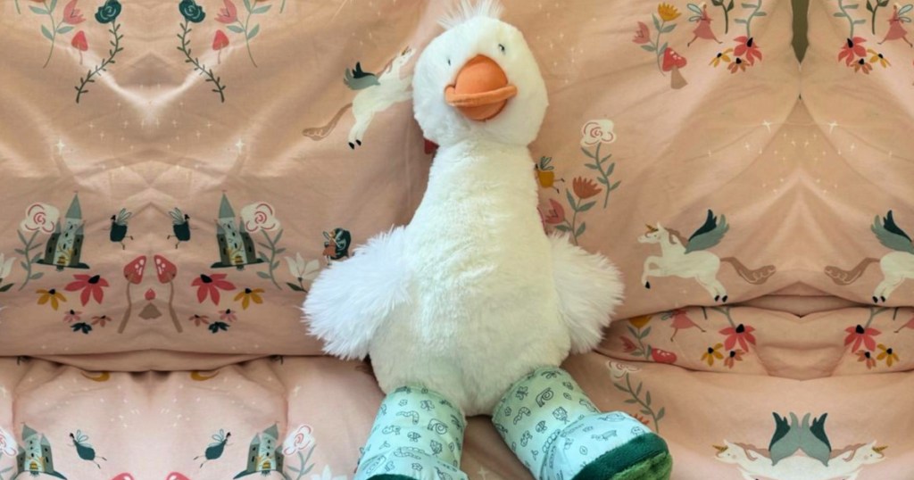 Duck plush wearing boots sitting on bed