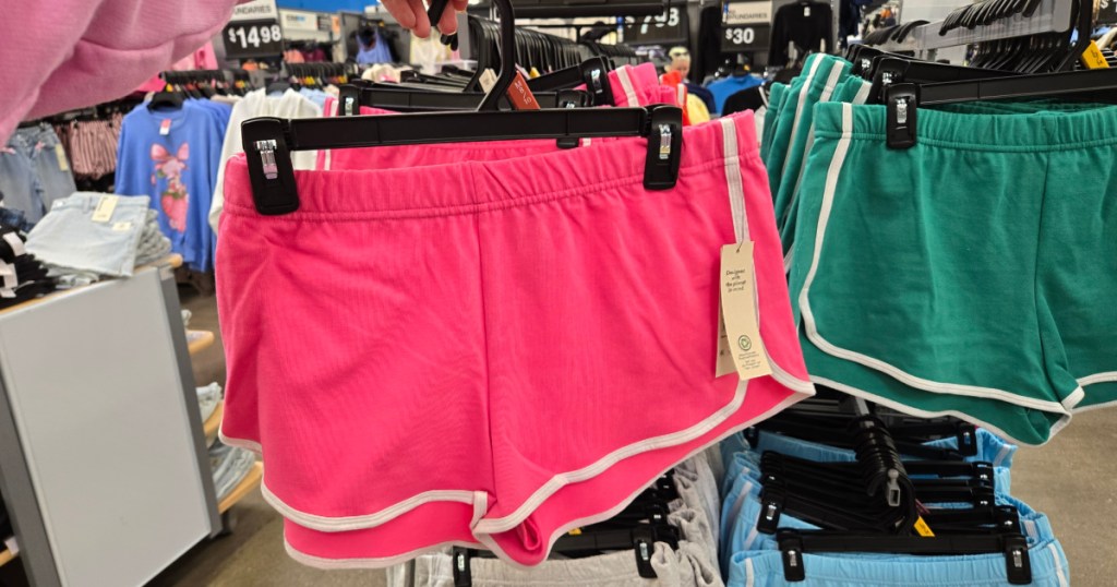 Woman holding up pink no boundaries shorts inside Walmart store