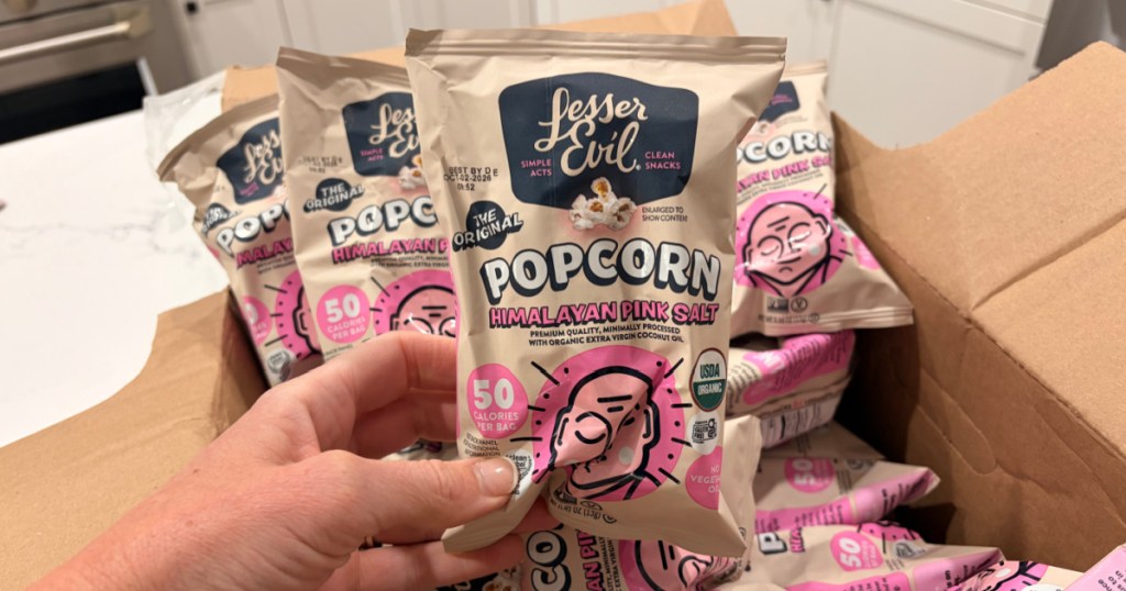 Woman holding up lesser evil popcorn, snack bags