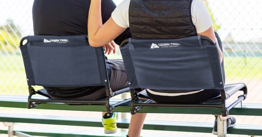two people sitting in navy blue stadium seats on bleachers