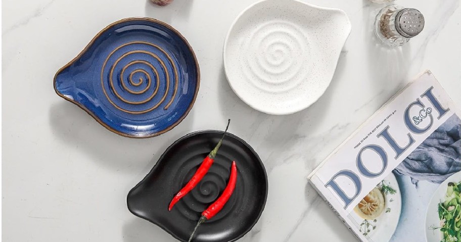 Three spiral-patterned dishes&mdash;blue, white, and black&mdash;are arranged on a marble surface. Red chili peppers rest on the black dish next to a magazine and salt shaker.