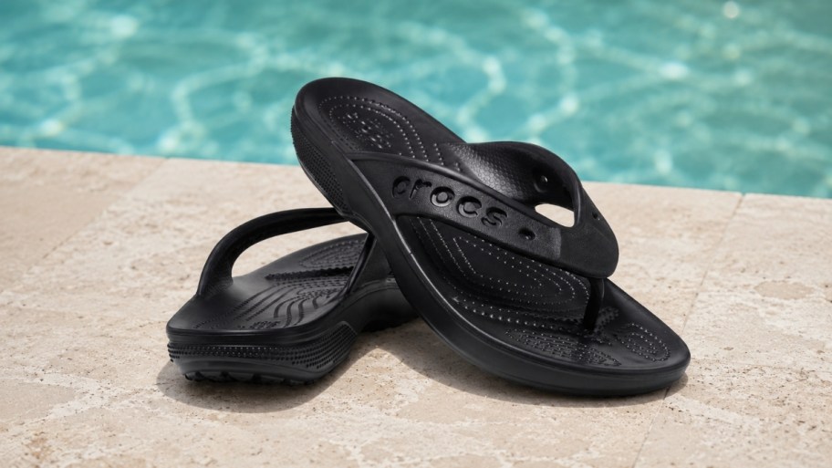 a pair of black crocs flip flops next to a pool