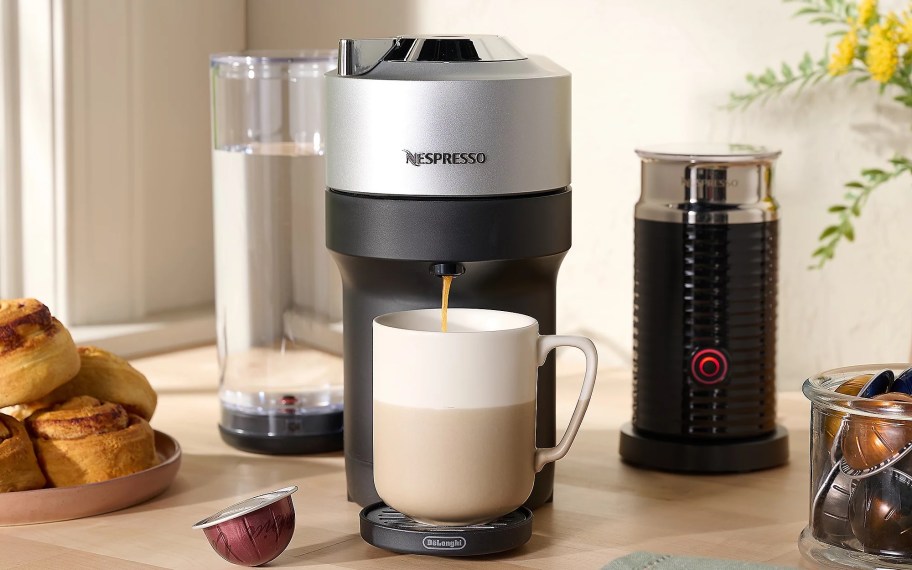 Nespresso coffee maker with cup of coffee, coffee capsules, and frother sitting on counter