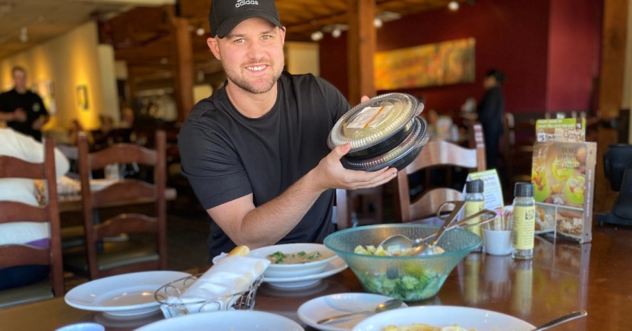 man at Olive Garden with plates of food on a table, holding to-go containers of food
