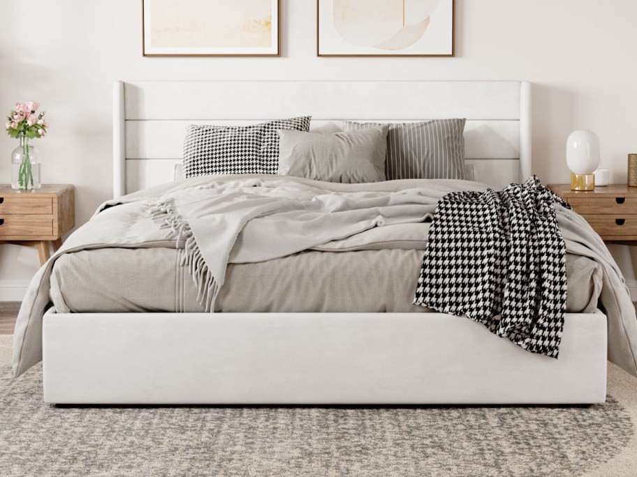 A neatly made bed with grey bedding and a houndstooth throw stands between wooden nightstands.