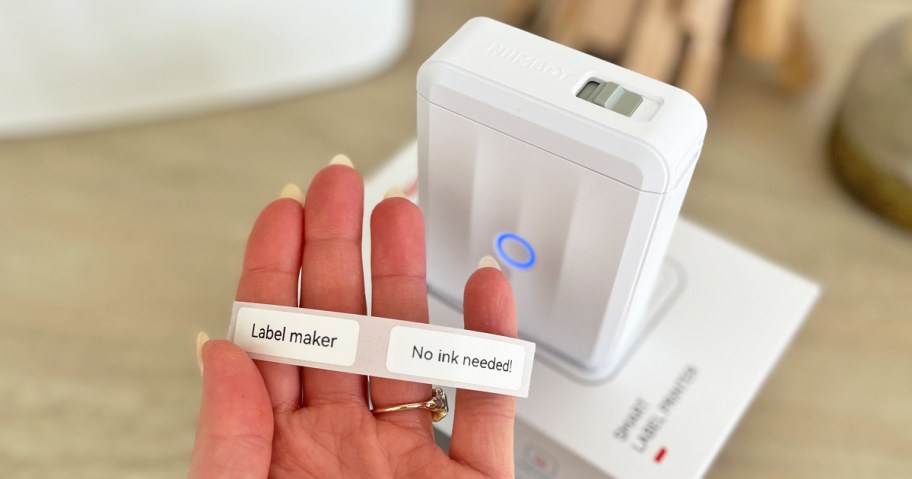 hand holding a strip of labels next to a white label printer