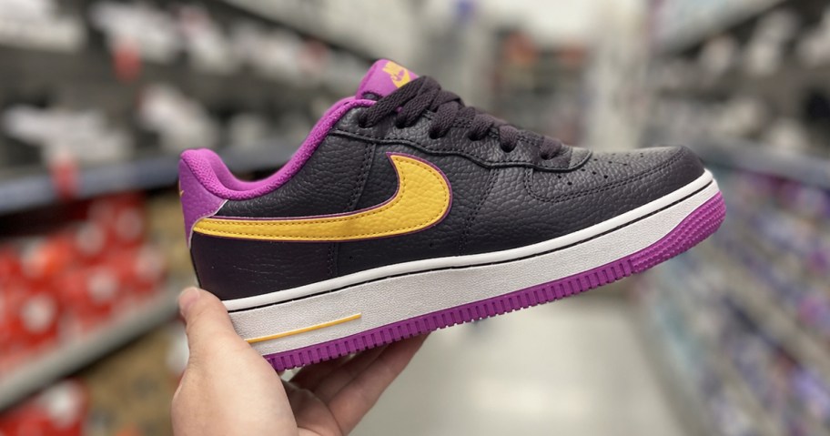 hand holding up a black, purple, and yellow nike shoe in store