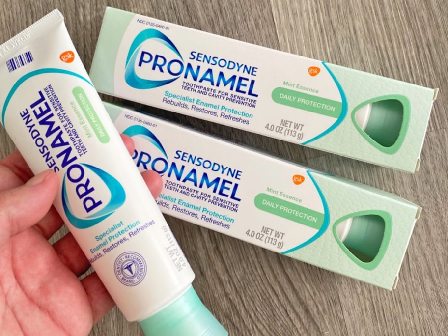 hand holding a tube of Sensodyne Pronamel Toothpaste with two more boxes in the background