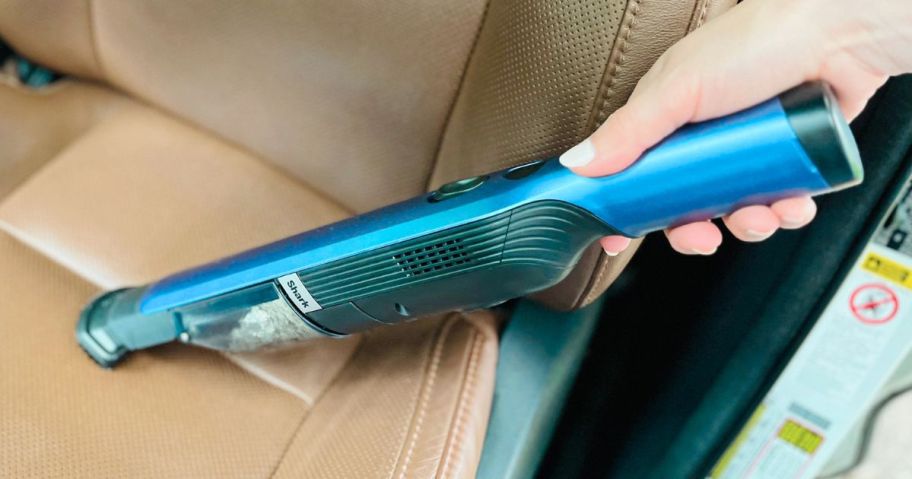 Hand using a Shark Wandvac to clean the front seat of a car