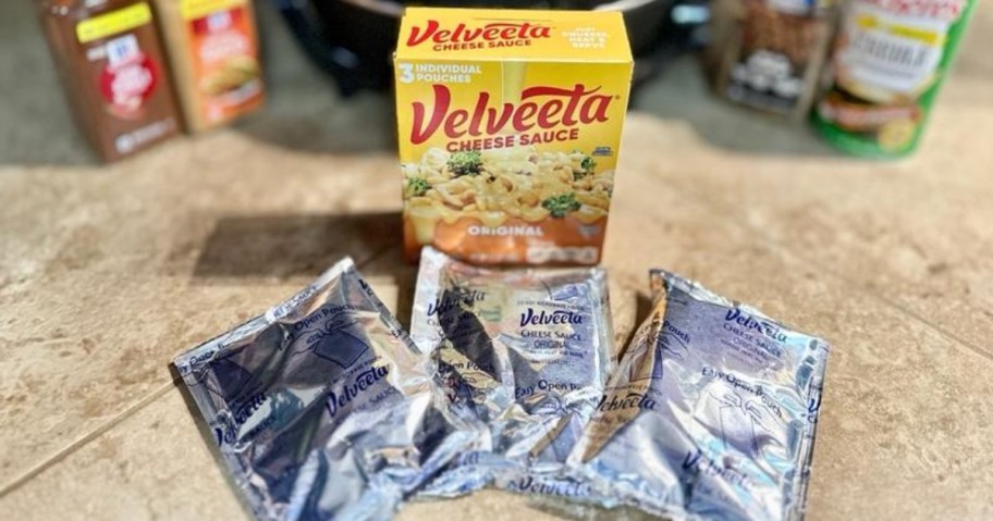 box of original velveeta cheese sauce on counter with three pouches of cheese laid out in front of it