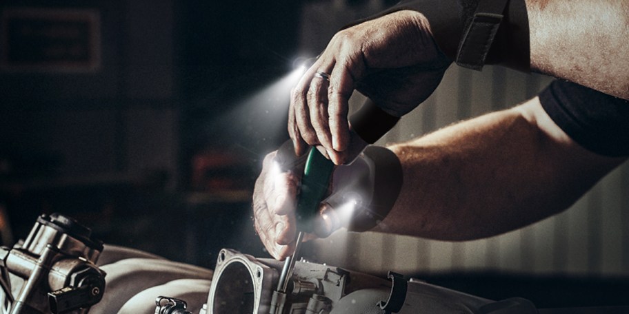 hands with flashlight gloves on working on car 