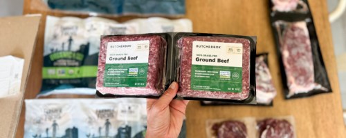 hand holding frozen ground beef above other meats