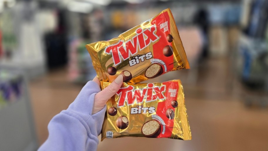 a womans hand holding two snack size bags of twix bits